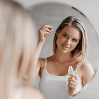 AHA Peeling Concentrate – Frau trägt das Peeling vor dem Spiegel mit Pipette auf