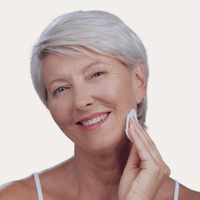 Hydrating Toner – ältere Frau mit grauem Haar reinigt ihr Gesicht mit Wattepad