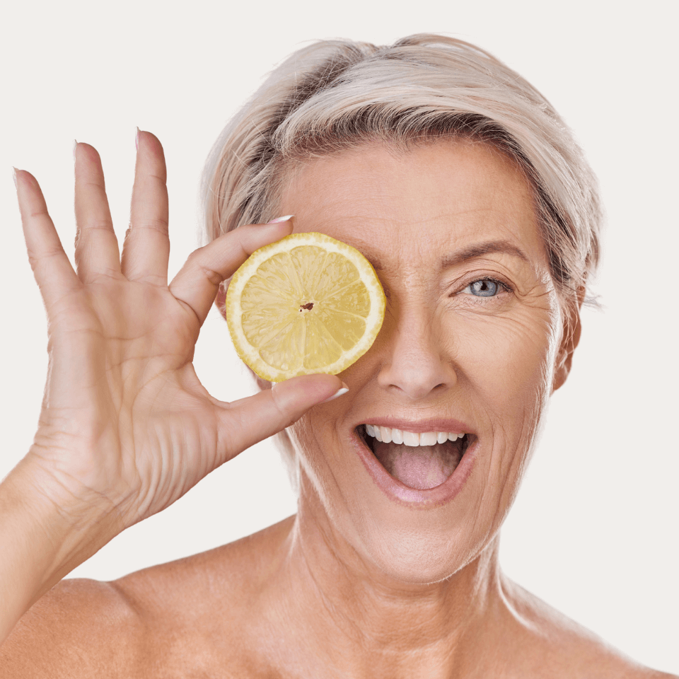 Vitamin C Serum – lachende Frau hält eine Zitronenscheibe vor ihr Auge