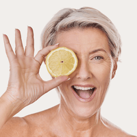 Vitamin C Serum – lachende Frau hält eine Zitronenscheibe vor ihr Auge